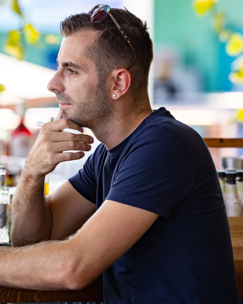 Oliver Albrecht at a bar in Cyprus, thinking, hand resting on his chin